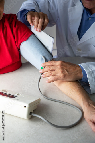 From above of crop physician with stethoscope sitting at table in medical room and measuring blood pressure with tonometer while working in hospital during coronavirus outbreak photo