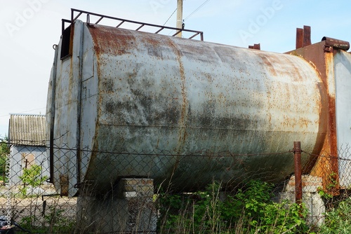one old iron gray tank in brown rust behind a metal fence on a street