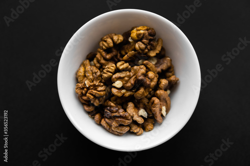 Walnut in a small plate on a black table. Walnuts is a healthy vegetarian protein nutritious food. Natural nuts snacks.
