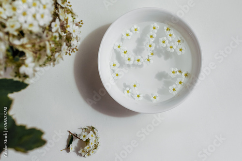 flowers floating in a water in white bowl. framing with bouqet. spa concept. top view.