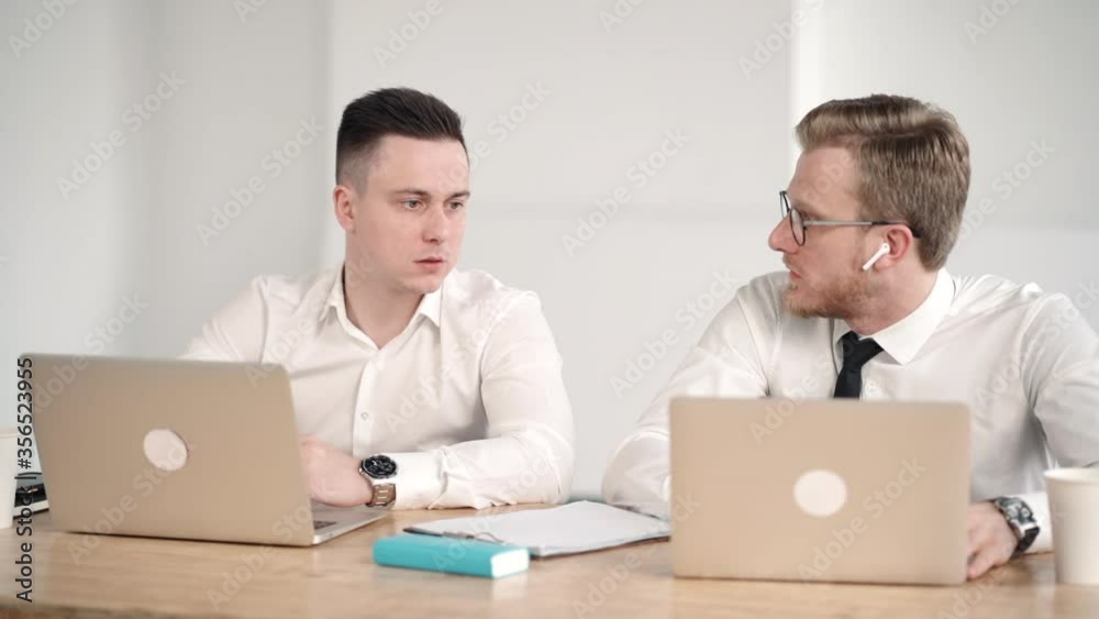 team of two businessmen in office discussing project. male colleague talking gives advice help. concept collaboration, successful, chatting. laptops on desk. white office team of two businessmen in office discussing project. male colleague talking gives advice help. concept collaboration, successful, chatting. laptops on desk. white office