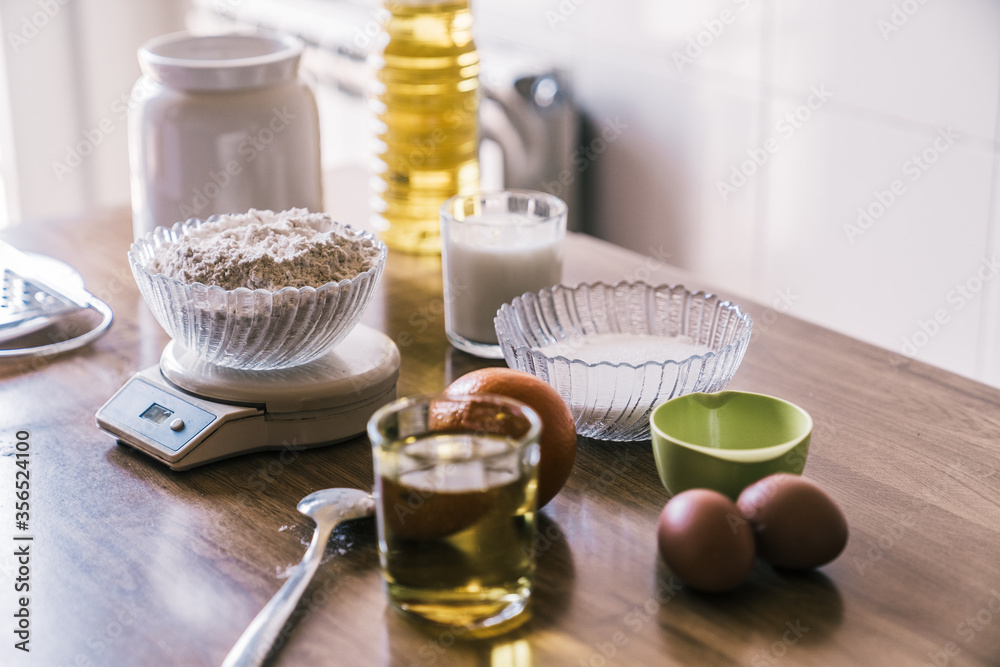 Ingredients for preparing homemade aromatic orange muffins placed on wooden counter near window in modern kitchen Ingredients for preparing homemade aromatic orange muffins placed on wooden counter near window in modern kitchen