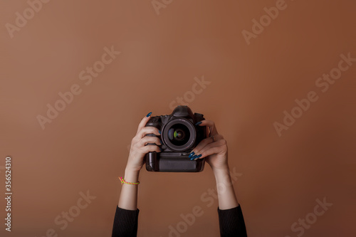 Photographer girl shooting images. Woman hands holding camera taking photos. Vivid brown background. World photography day. Studio photography. Space for text. Top view, minimalism
