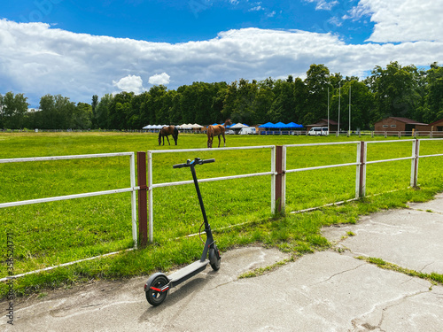 Horse in the arena. In the stall is a beautiful white horse. An electric scooter is parked near the horse arena. Animal and electric transport. Past and future are near. Eco friendly mobility concept