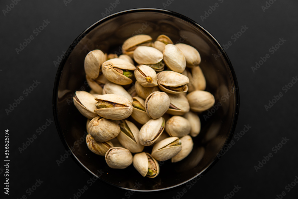 Pistachios in a small plate on a black table. Pistachio is a healthy vegetarian protein nutritious food. Natural nuts snacks. Pistachios in a small plate on a black table. Pistachio is a healthy vegetarian protein nutritious food. Natural nuts snacks.