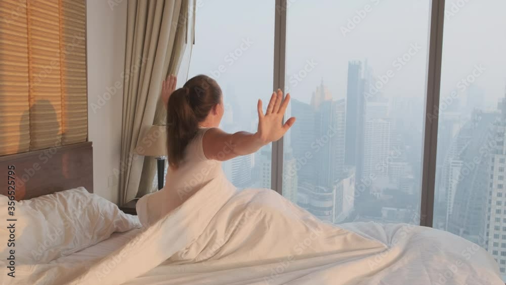 custom made wallpaper toronto digitalwoman wakes up stretching while sitting on bed in bedroom looking out window at city on sunny morning.