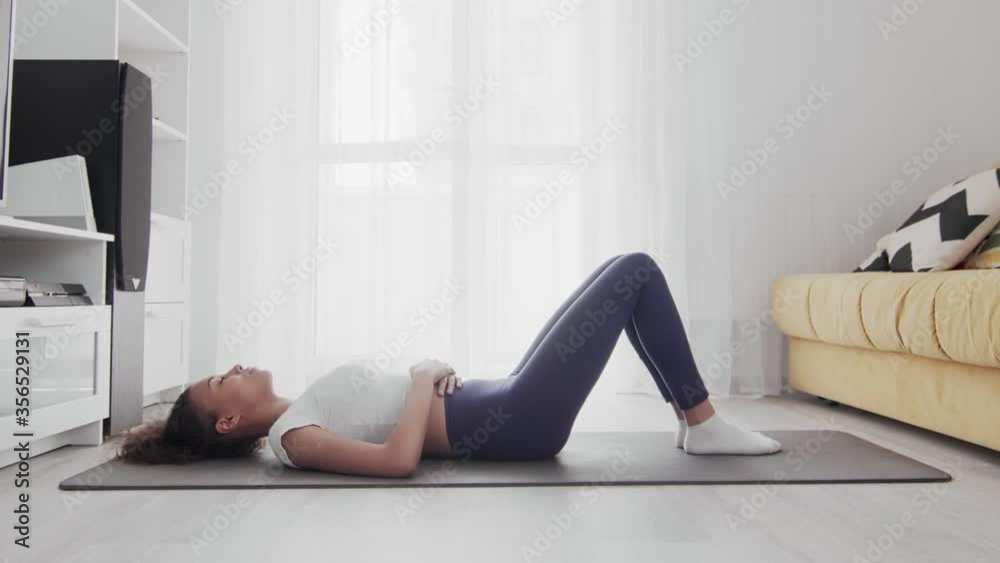 Young sporty african american woman lays on mat and haves a rest after exercises at home