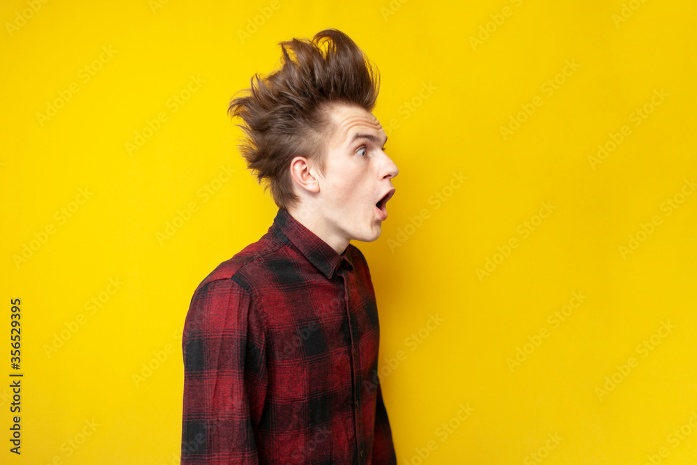 young shocked guy surprised at yellow isolated background, hipster with funny hairstyle screaming to the side