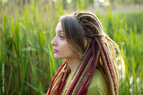 Outdoors portrait of a girl with dreadlocks and green shirt in a city park near the lake during a sunset  be free concept.