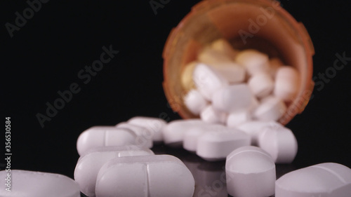 Prescription drugs poured out onto black table top scattered over the surface.