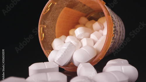 Opioids lying on black table top with open bottle looking into bottle.