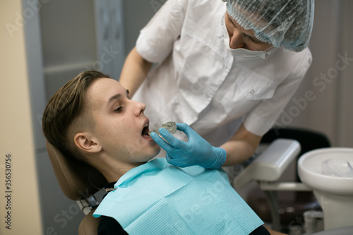 Female dentist puts on a guy patient a removable orthodontic teeth alignment in dental office.