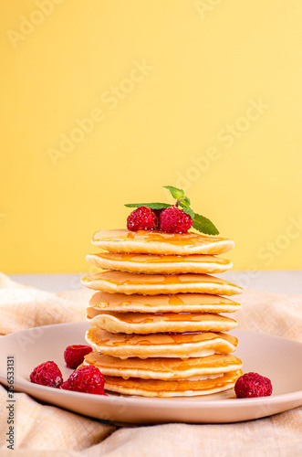 Homemade classic American pancakes with fresh raspberries, blackberries, honey and mint leaves, on a light background.