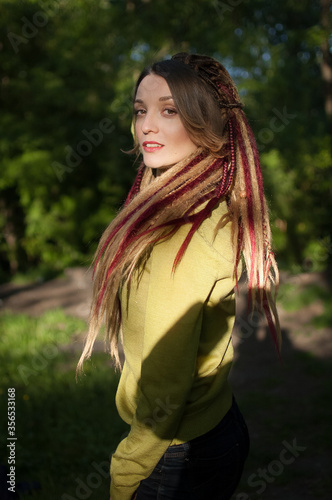 Outdoors portrait of a sensual girl with long dreadlocks wearing green shirt in a city park during a sunset, be different, alternative people concepts