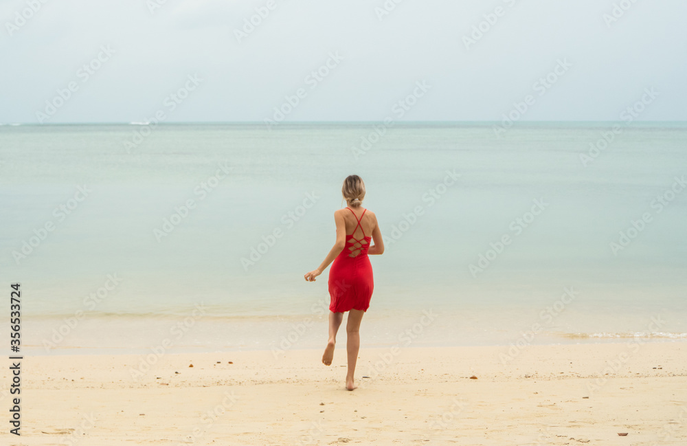 Young woman in a red dress runs and jumps on a white sand beach into tropical sea. Young happy woman running on the beach. Happiness to be on a sea or ocean. Vacation and travel concept. Young woman in a red dress runs and jumps on a white sand beach into tropical sea. Young happy woman running on the beach. Happiness to be on a sea or ocean. Vacation and travel concept.