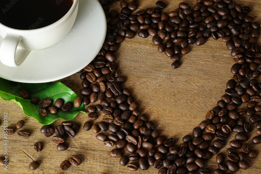 Naklejka premium White coffee cup and coffee beans on wooden table with heart copyspace for text. Selective focus.