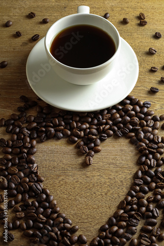 White coffee cup and coffee beans on wooden table with heart copyspace for text. Selective focus.