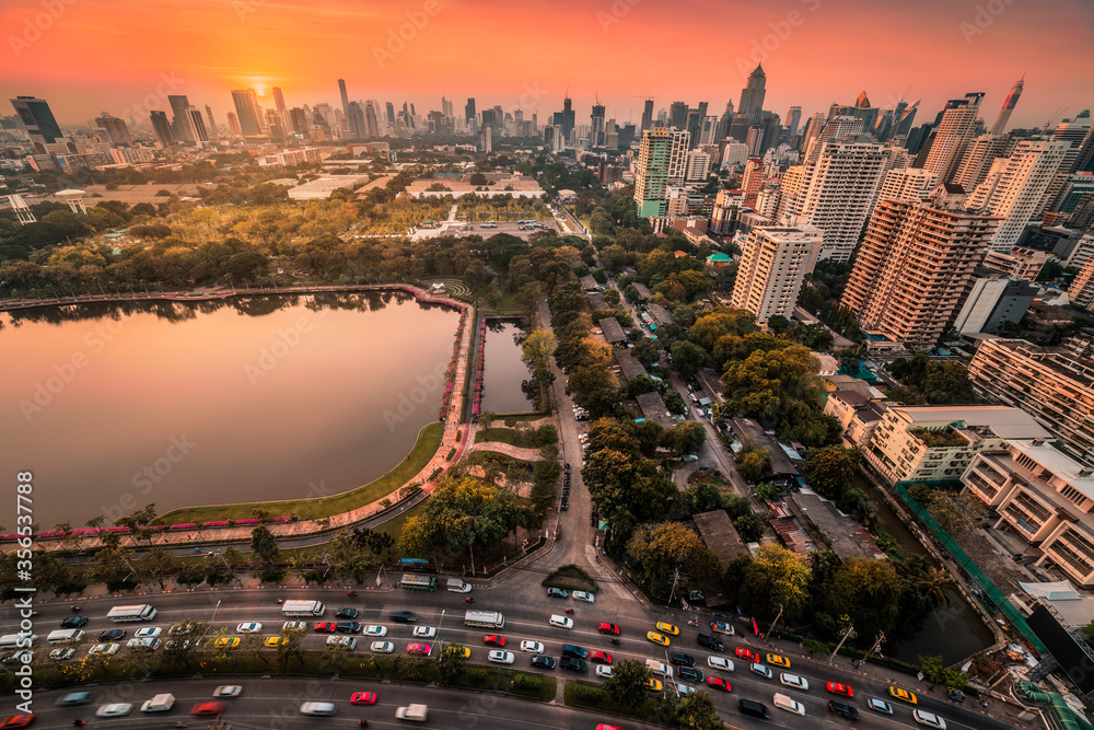 Fototapeta premium Benjakiti Public Park with a Lake, Skyscrapers and Traffic in Bangkok, Thailand at Sunset