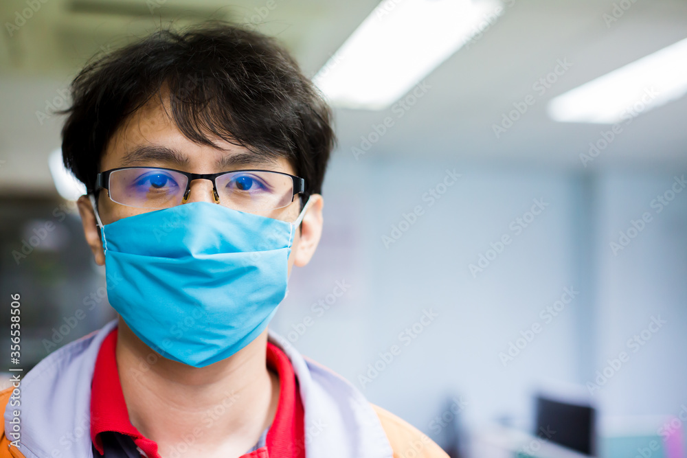 Asian man wears glasses and a face mask that protects against the spread of Coronavirus disease. Close up of a young man wearing a surgical mask on his face against Covid-19.