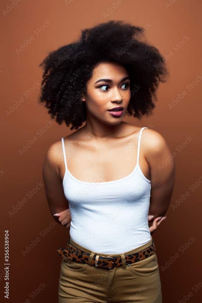 pretty young african american woman with curly hair posing cheerful gesturing on brown background, lifestyle people concept