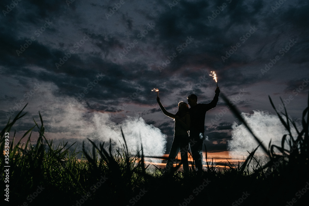 young loving having fun couple in a field with fireworks far from all silhouette