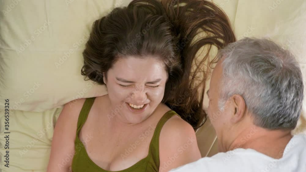 Happy funny young family couple laughing on bed mattress, active carefree husband and wife having fun laughing enjoying honeymoon party together in morning or night in cozy bedroom. Man making tickles Happy funny young family couple laughing on bed mattress, active carefree husband and wife having fun laughing enjoying honeymoon party together in morning or night in cozy bedroom. Man making tickles