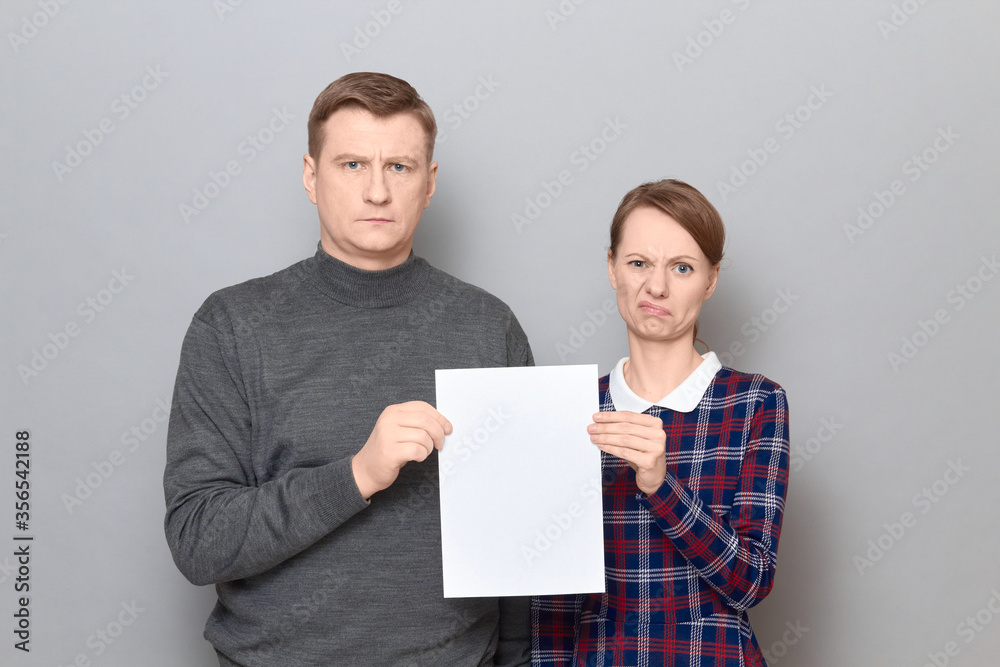 Portrait of adult couple holding together white blank paper sheet Portrait of adult couple holding together white blank paper sheet