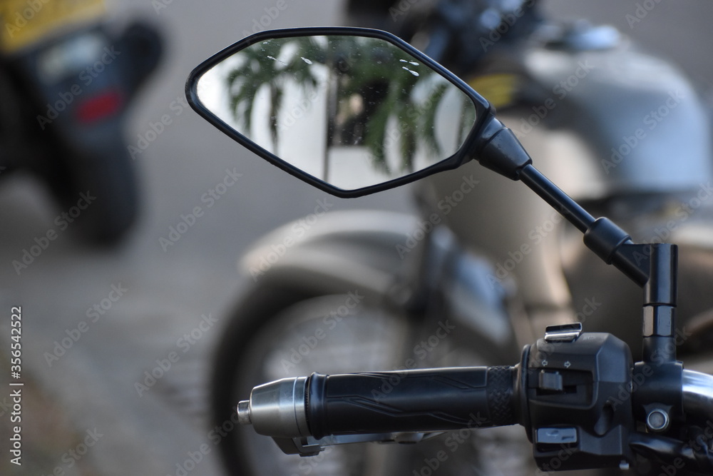 Espejo de una motocicleta ubicada junto a su respectivo mango, reflejando palmeras de forma borrosa. Espejo de una motocicleta ubicada junto a su respectivo mango, reflejando palmeras de forma borrosa.