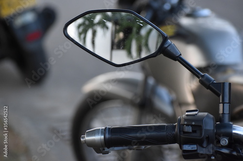 Espejo de una motocicleta ubicada junto a su respectivo mango, reflejando palmeras de forma borrosa.