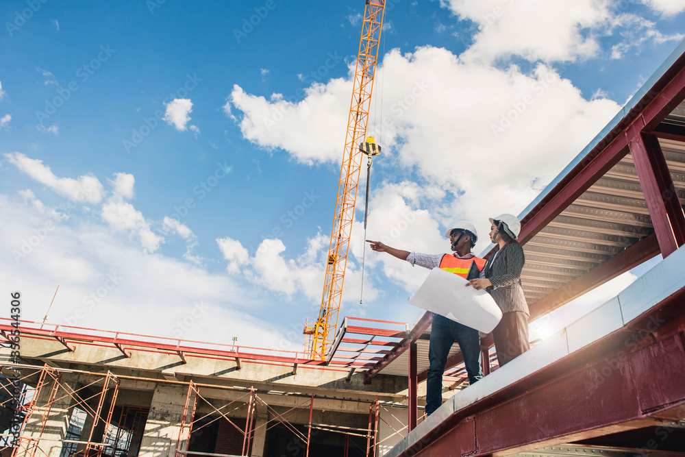 Naklejka premium Engineer in hardhat and orange jacket posing on building site. civil engineer or architect with hardhat on construction site checking schedule on plan.