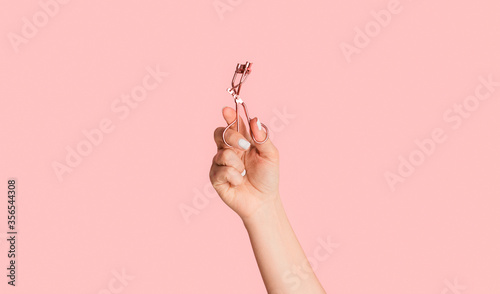 Closeup of beautician hand holding eyelash curler on pink background