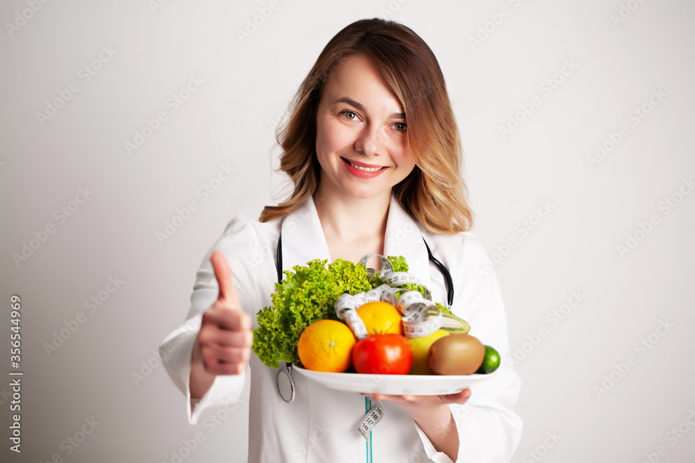 A young nutritionist holding in her hands fresh vegetables and fruits on plate in the consultation room A young nutritionist holding in her hands fresh vegetables and fruits on plate in the consultation room