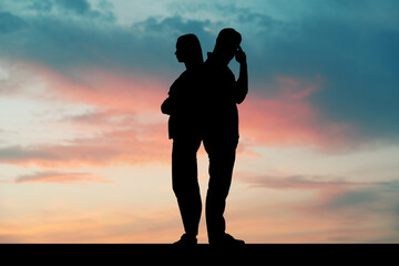 Silhouettes of arguing couple against sunset sky with clouds. Relationship problems