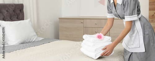 Chambermaid putting fresh towels on bed in hotel room, closeup view with space for text. Banner design photo