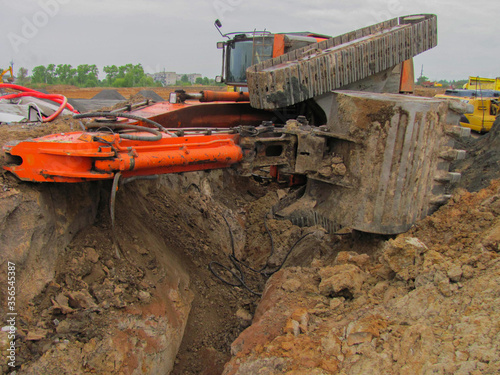 Construction accident. A large orange excavator has overturned near a trench at a construction site, creating a hazardous situation.