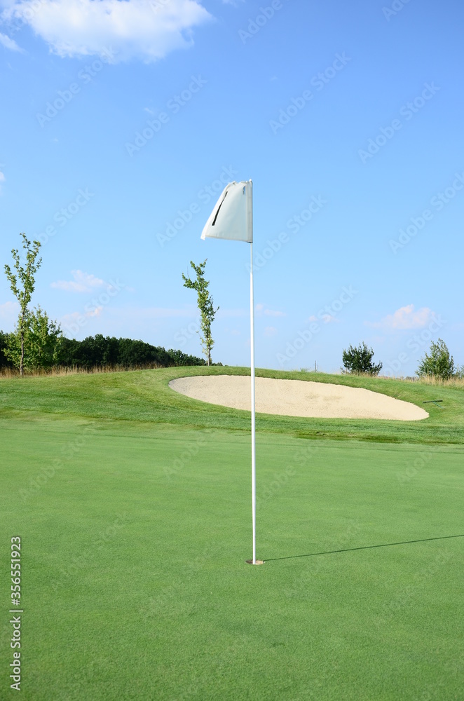 Obraz premium golf flag on green grass agains blue sky