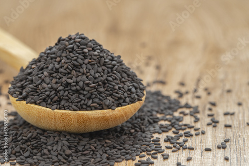 Black dried sesame seeds on wooden spoon over wood table.