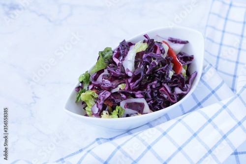   Red cabbage salad. fresh vegetable salad in white ceramic plates and checkered cotton napkin on a light marble background.Vegetable salad ingredients.Healthy eating and diet. © Yuliya