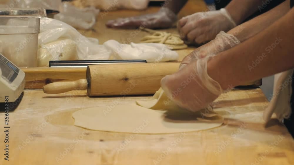 Someone's making dough on a wooden table. The chef is rolling out the dough in the restaurant kitchen. Hands wrinkle the dough. Food video close up kitchen. Someone's making dough on a wooden table. The chef is rolling out the dough in the restaurant kitchen. Hands wrinkle the dough. Food video close up kitchen.