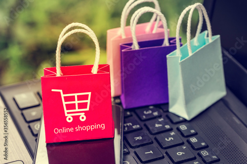 Colorful paper shopping bags with mobile phone on a laptop keyboard. Concept about online shopping that customers can buy everything from home or office. Via the tool electronics.