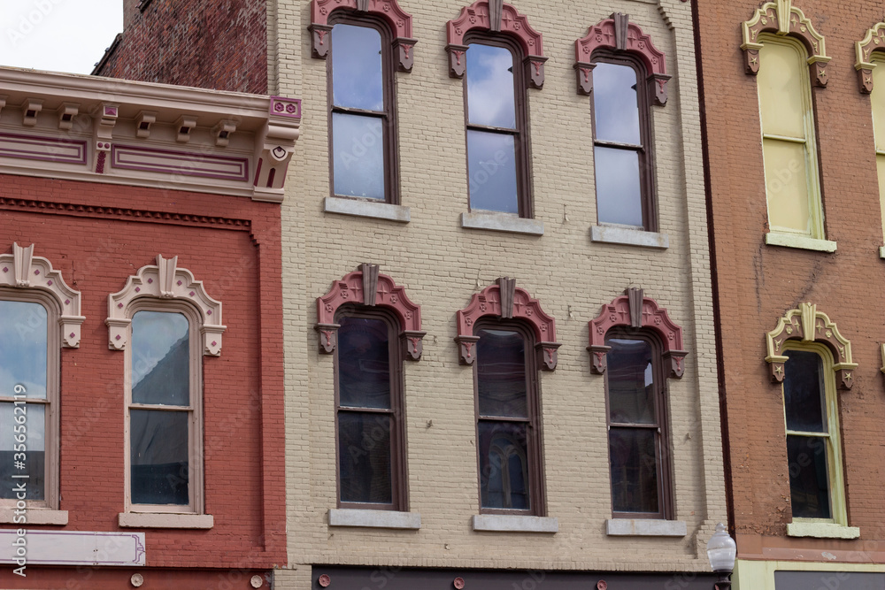 Close upward view of tall windows on old urban building brick walls with beautiful ornate wood moulding
