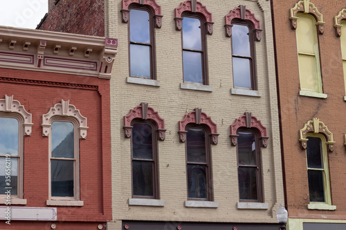 Close upward view of tall windows on old urban building brick walls with beautiful ornate wood moulding