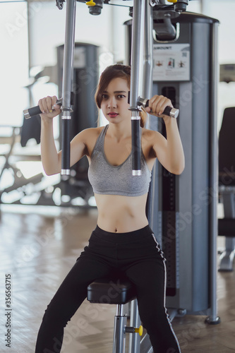 Fototapeta Naklejka Na Ścianę i Meble -  fitness new normal, Woman at the gym on a sports simulator., Fit beautiful young woman exercise workout on machine in gym. Glad smiling girl is enjoy with her training process. Concept of fitness, Hea