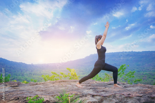 Young woman standing and doing yoga pose at the top of mountain in the morning 
