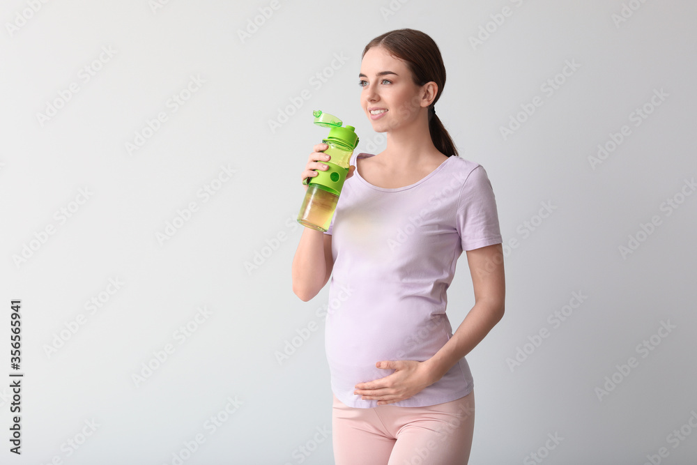Young pregnant woman with bottle of water on light background - obrazy, fototapety, plakaty 