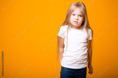 A girl stands with a questioning facial expression on an orange background. The child depicts emotions