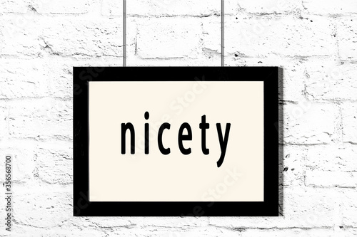 Photography Black frame hanging on white brick wall with inscription nicety