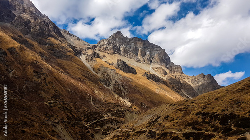 Harsh and golden colored slopes in Manang Valley, Annapurna Circus Trek, Himalayas, Nepal, with the view on Annapurna Chain and Gangapurna. Dry and desolated landscape. High snow capped mountain peaks