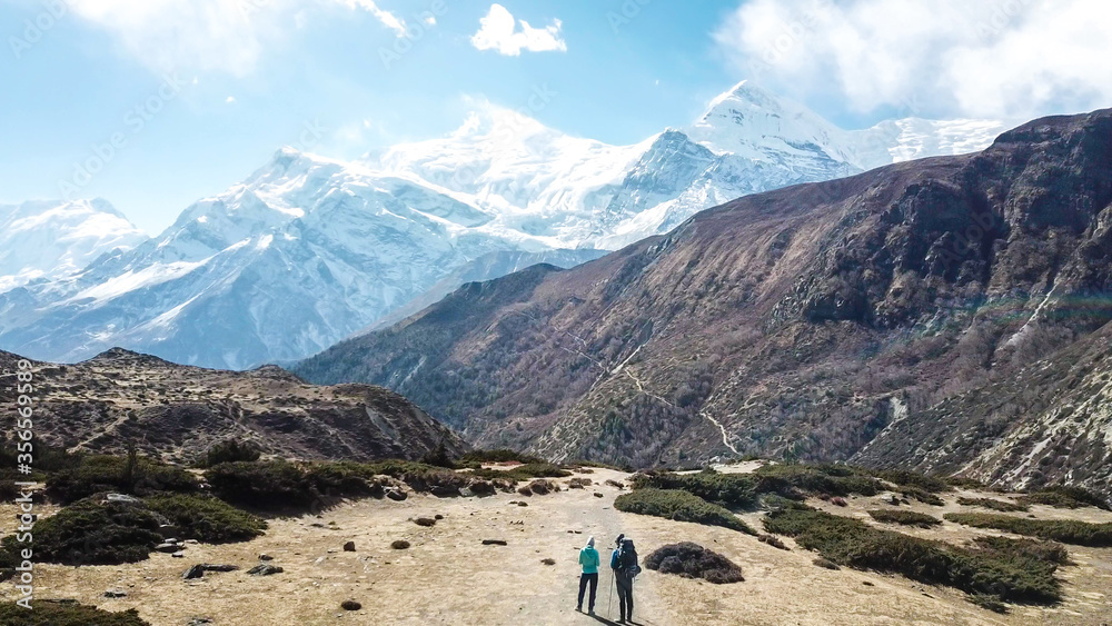 A couple trekking in the Manang Valley, Annapurna Circus Trek, Himalayas, Nepal, with the view on Annapurna Chain and Gangapurna. Dry and desolated landscape.  High snow capped mountain peaks. Freedom