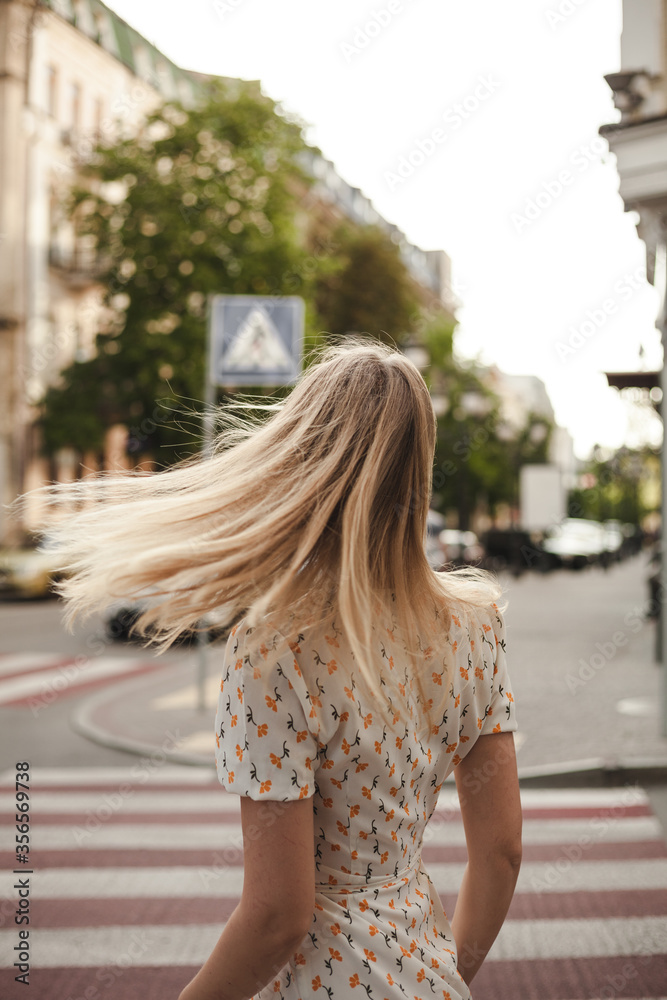 Portrait photo of a girl from the back against the backdrop of the city landscape. Girl blonde on a summer day walks in the city
